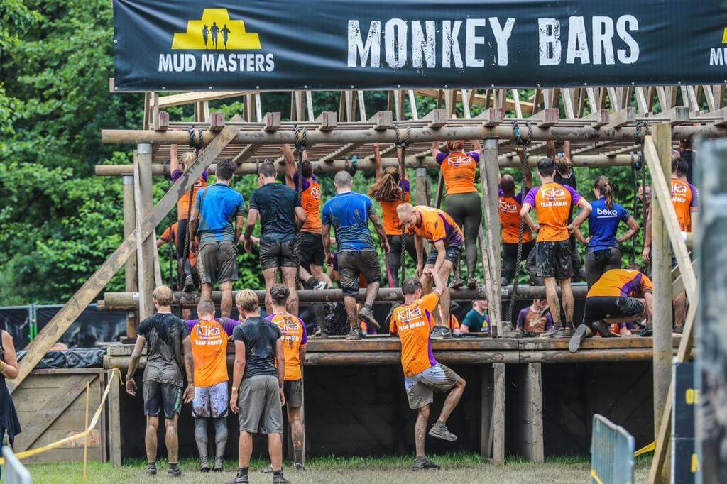 Mud Masters deelnemers klimmen en balanceren op modderige monkey bars tijdens het uitdagende obstacle run evenement.