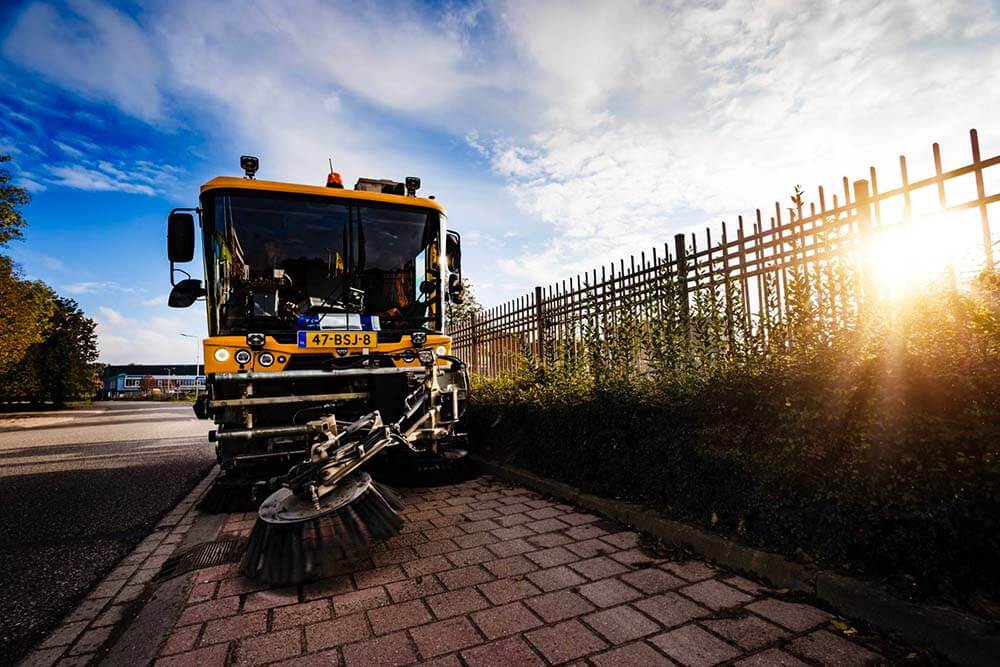 Veegmachine in actie op straat bij zonsondergang, onderdeel van terreinreiniging en schoonmaakdiensten van What A Waste.