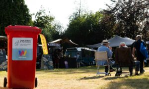 Rode rolcontainer met label van What A Waste geplaatst op een evenemententerrein, zonlicht schijnt op de container.