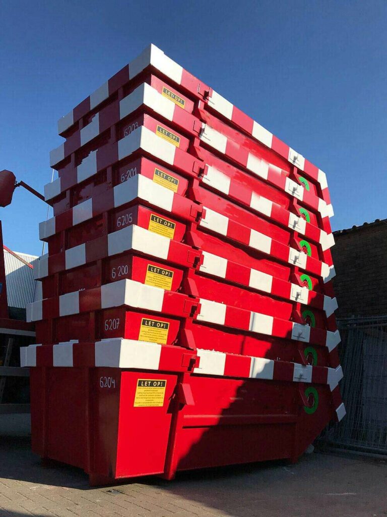 Stapel rode en witte afzetcontainers bij afvalbedrijf, met heldere waarschuwingen en herkenbare omgeving, onderdeel van containerverhuur door What A Waste.