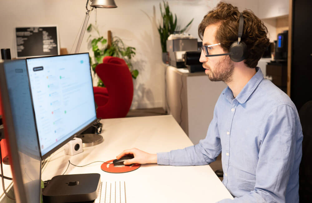 Medewerker van de helpdesk met headset werkt geconcentreerd achter computer om offertes voor What A Waste aan te vragen.